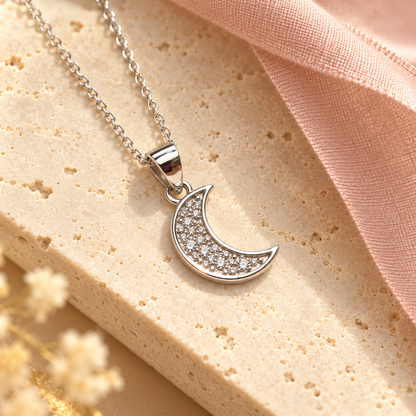 Silver crescent pendant displayed on an ivory travertine plinth with a blush ribbon.