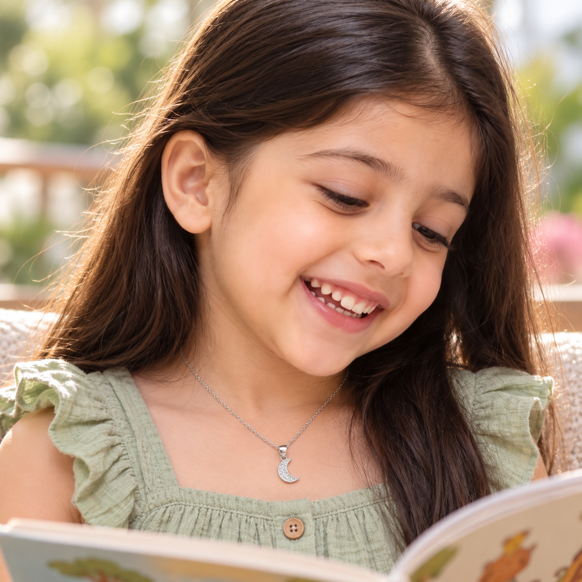 Child wearing a small silver crescent pendant while reading outdoors.