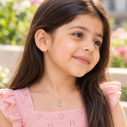 Close view of a child in a pink cotton dress wearing a sterling silver crescent pendant.