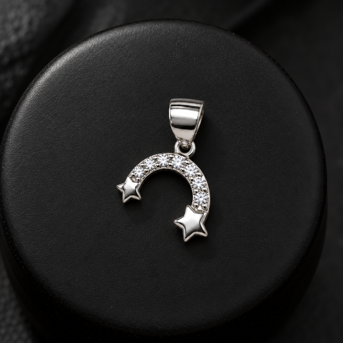 Silver arch pendant on a matte black ceramic pedestal with crisp highlight reflections.