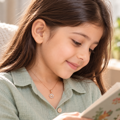 Side view of a child quietly reading while wearing a rose gold sun pendant.