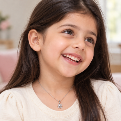 Child wearing a silver smiling sun pendant on a fine chain with a cream top.