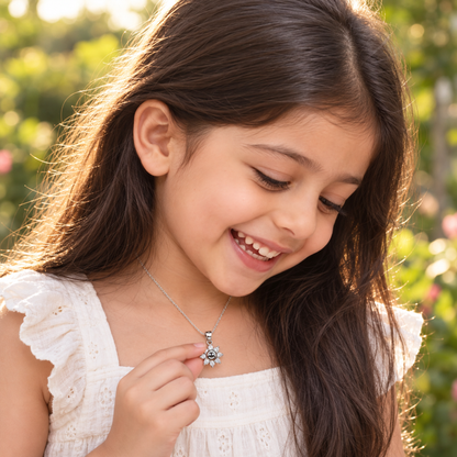 Child outdoors holding a delicate silver sun pendant in soft golden sunlight.