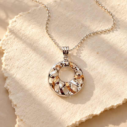 Two-tone silver and gold swirl pendant with a delicate chain on textured ivory paper.