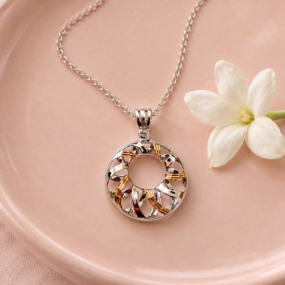 Circular swirl pendant resting on a blush pink ceramic plate next to a small white flower.