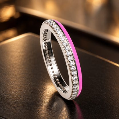 Silver cubic zirconia and pink enamel band ring displayed on a dark matte ceramic surface.