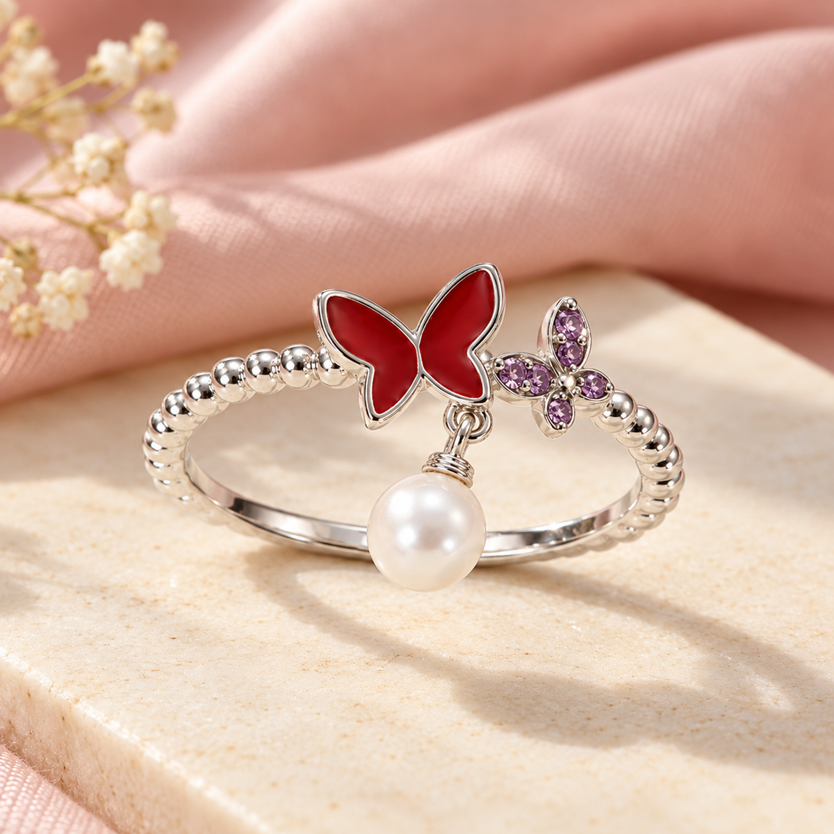 Sterling silver butterfly and pearl ring resting on an ivory stone tile with blush pink silk in the background.