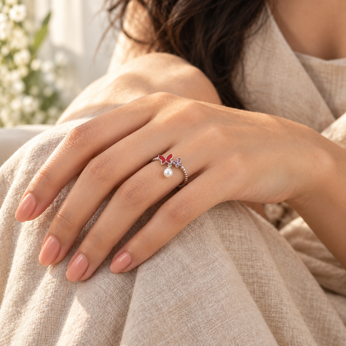 Close-up of a hand wearing the silver butterfly ring with a dangling pearl against a beige linen dress.