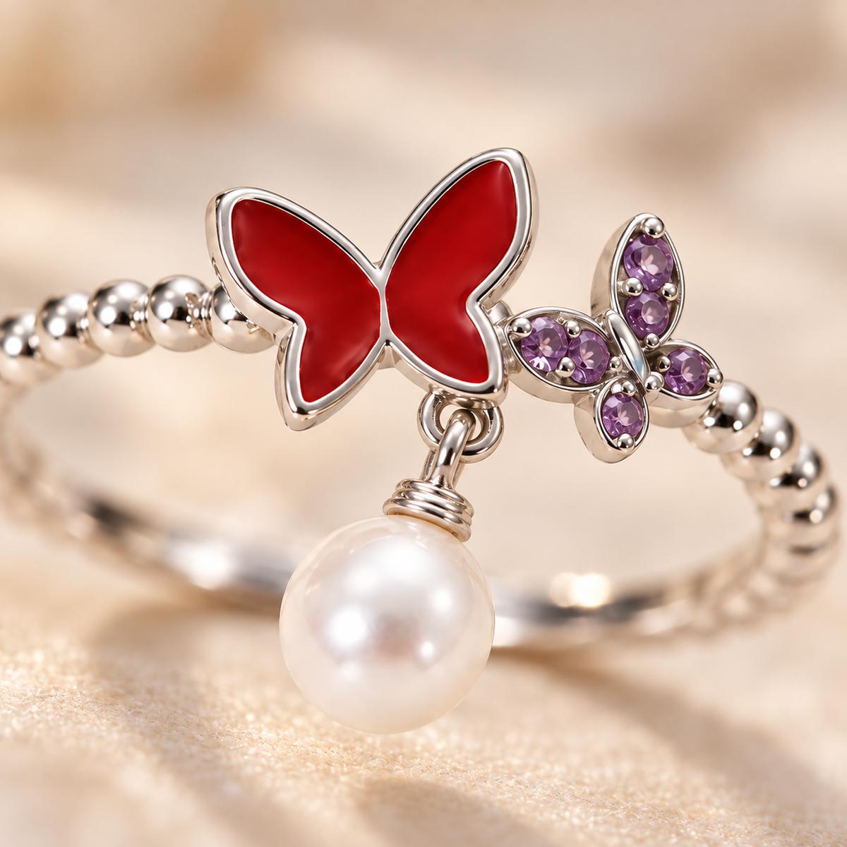 Macro detail shot of the red and purple enamel butterflies and the dangling white pearl on the silver ring.