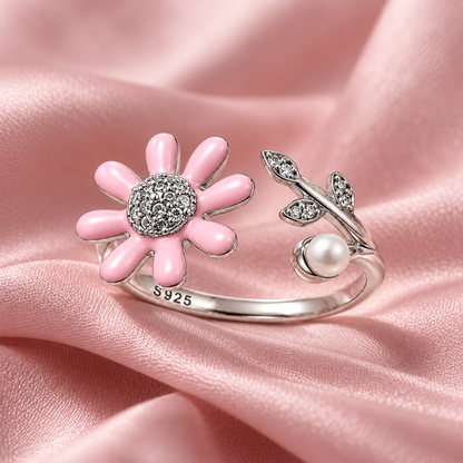 A silver daisy and pearl ring resting on draped blush pink silk fabric with soft shadows.
