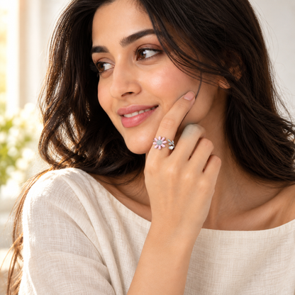 A close-up of a woman smiling softly, wearing a silver daisy and pearl ring on her index finger.