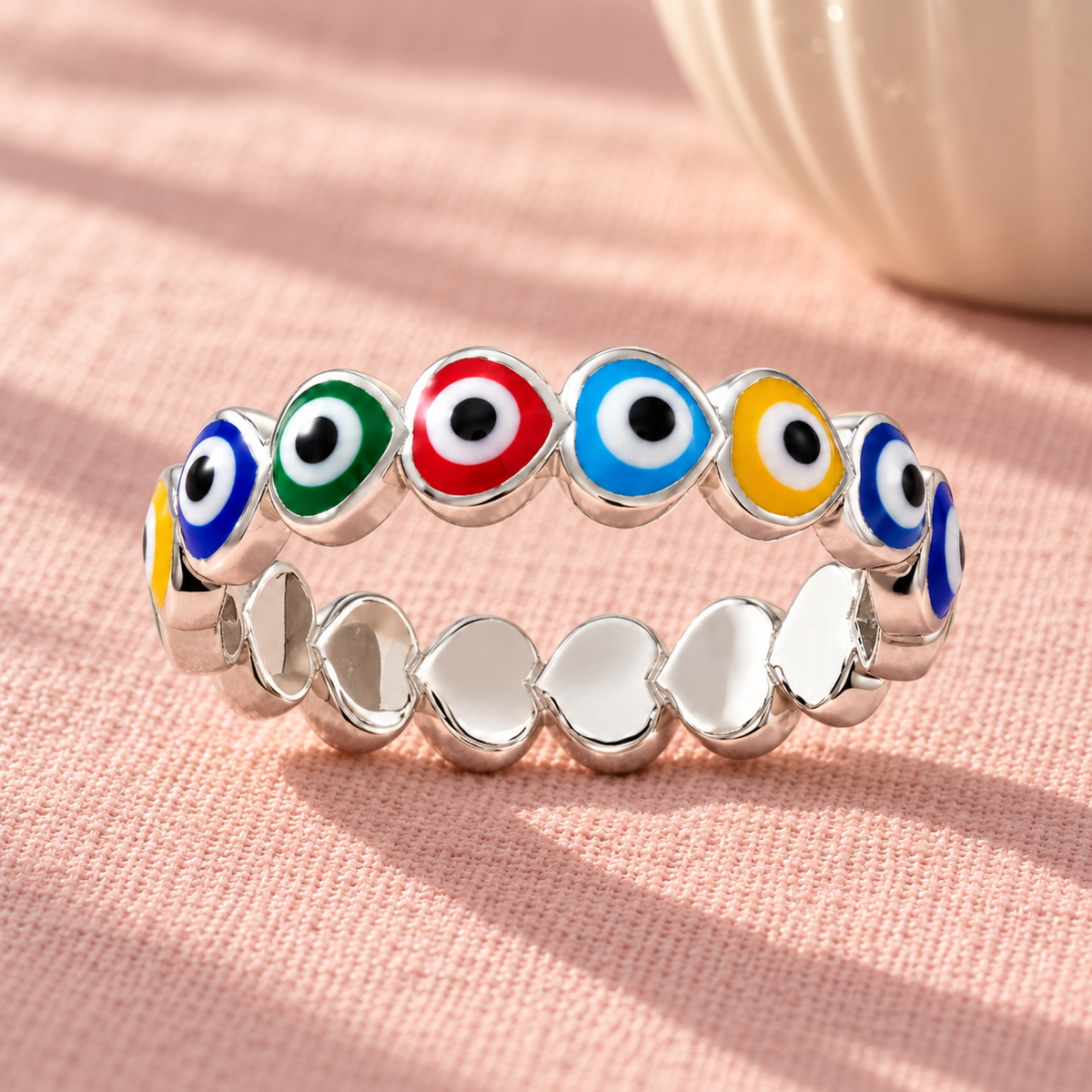 Silver evil eye heart ring on textured blush pink linen under soft morning sunlight.