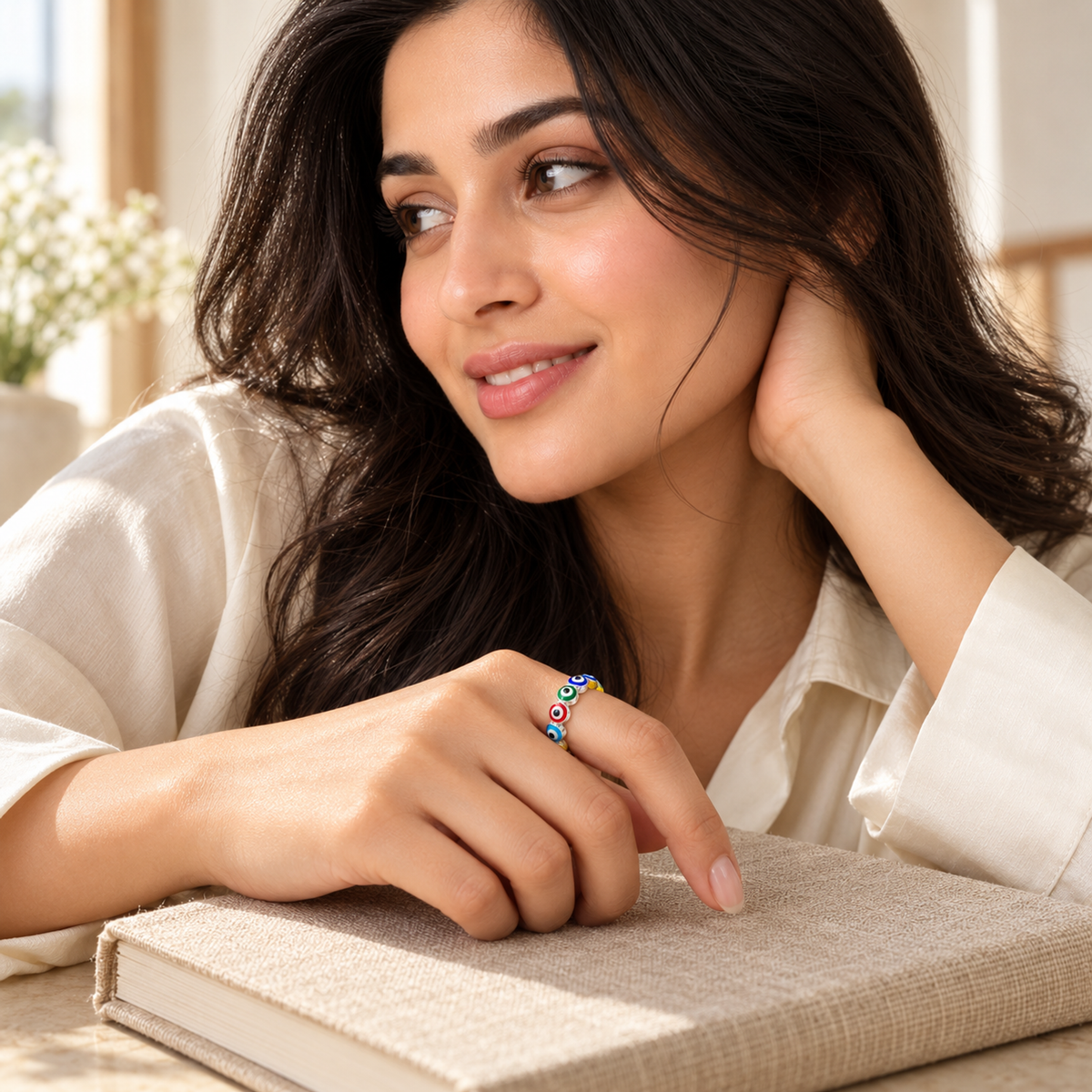 A hand wearing a silver heart eternity ring with colourful enamel details, resting on a beige book.