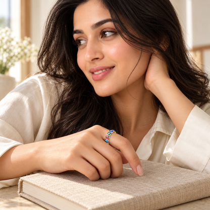 A hand wearing a silver heart eternity ring with colourful enamel details, resting on a beige book.