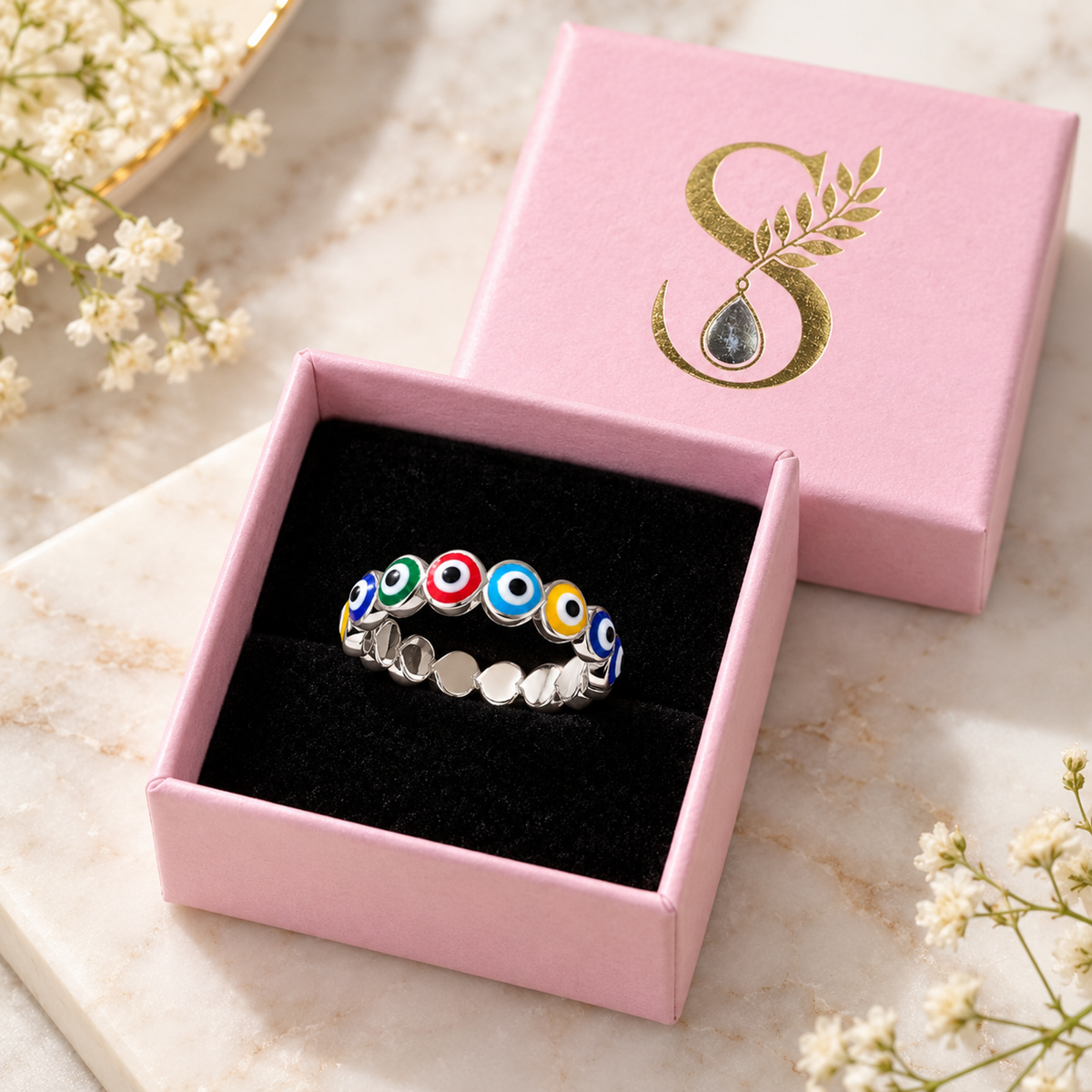 Silver heart ring with multicoloured enamel inside a pale pink box with a black velvet interior.