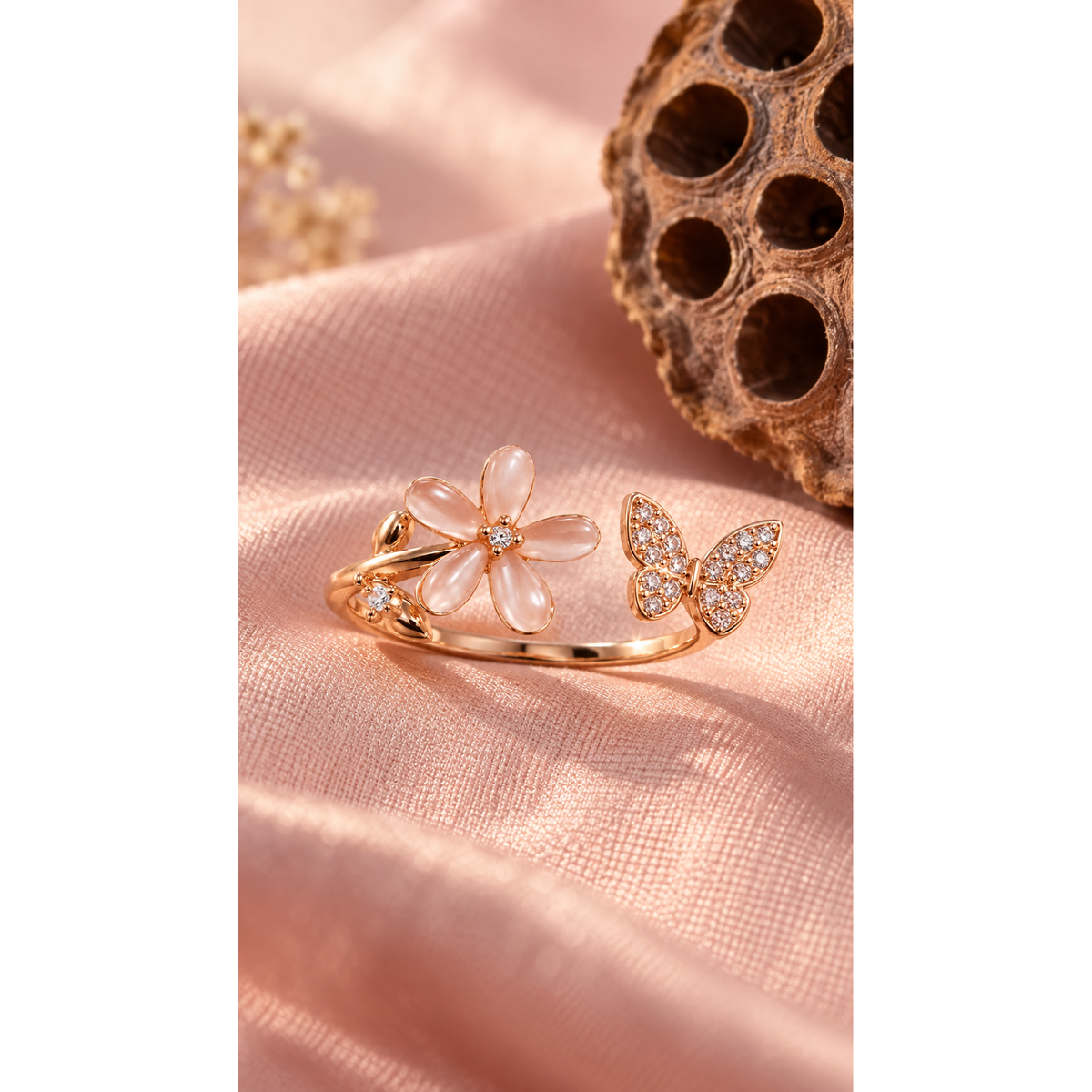 Rose gold flower and butterfly ring resting on blush pink silk in warm soft sunlight.