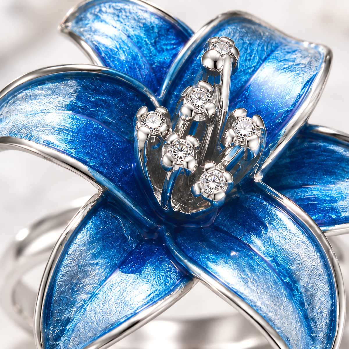 Macro close-up of blue enamel petals and stone-set stamens on a silver ring.