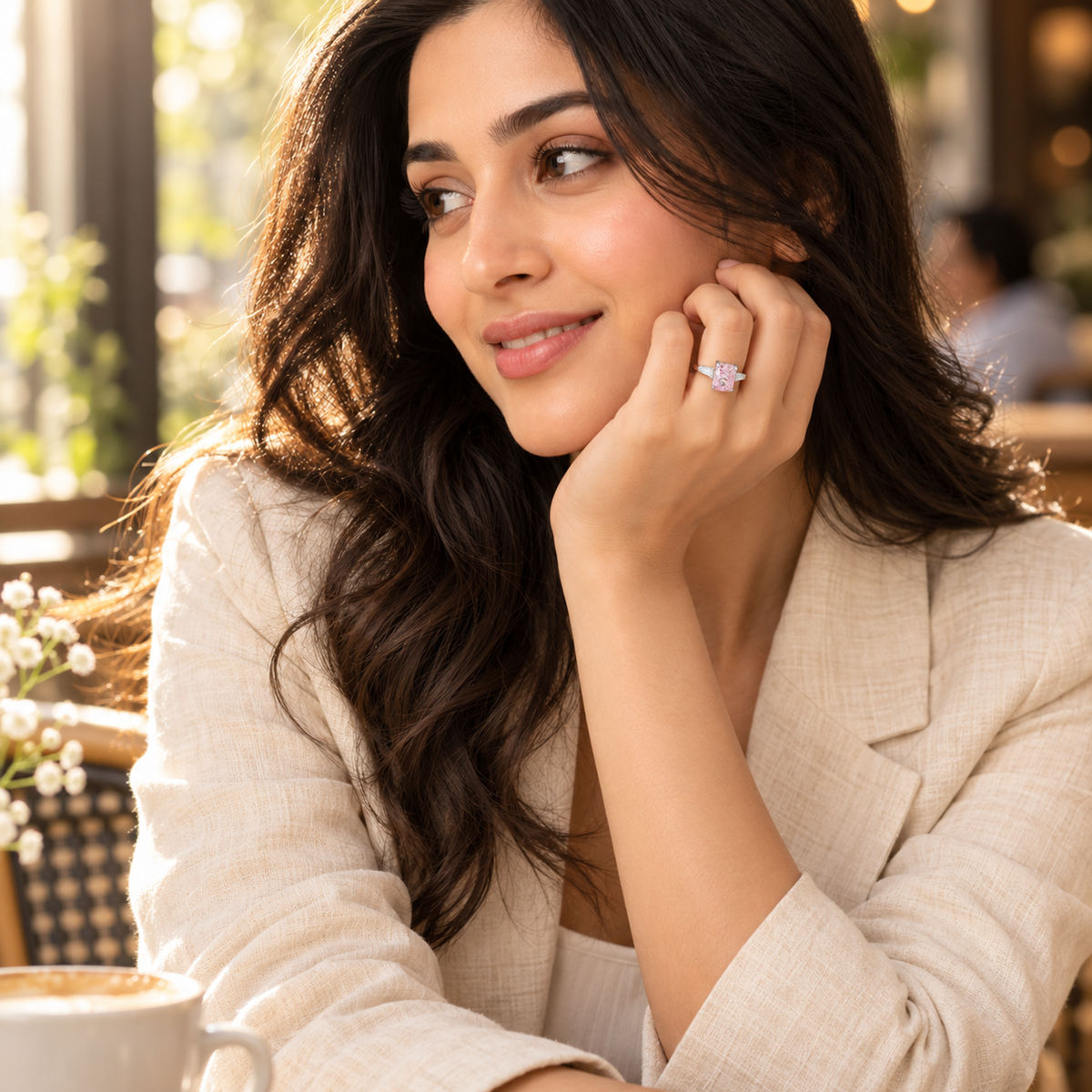 A woman wearing a silver ring with a pink gemstone, resting her hand on her cheek in warm sunlight.