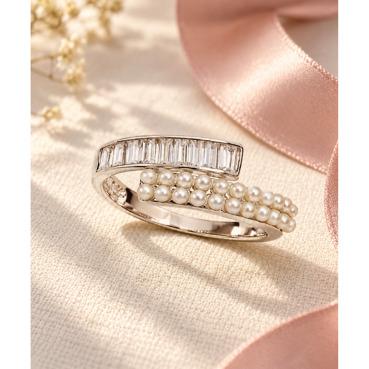 Silver bypass ring resting on ivory linen near a pink ribbon.