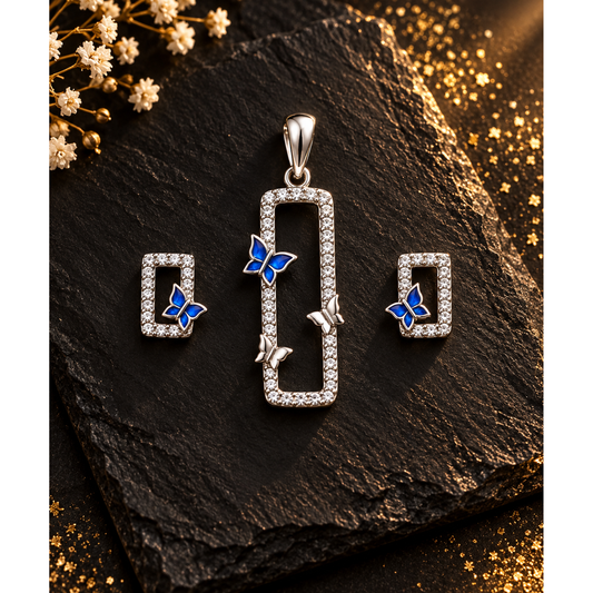 Silver rectangular pendant set with blue enamel butterflies on dark slate with soft warm lighting.
