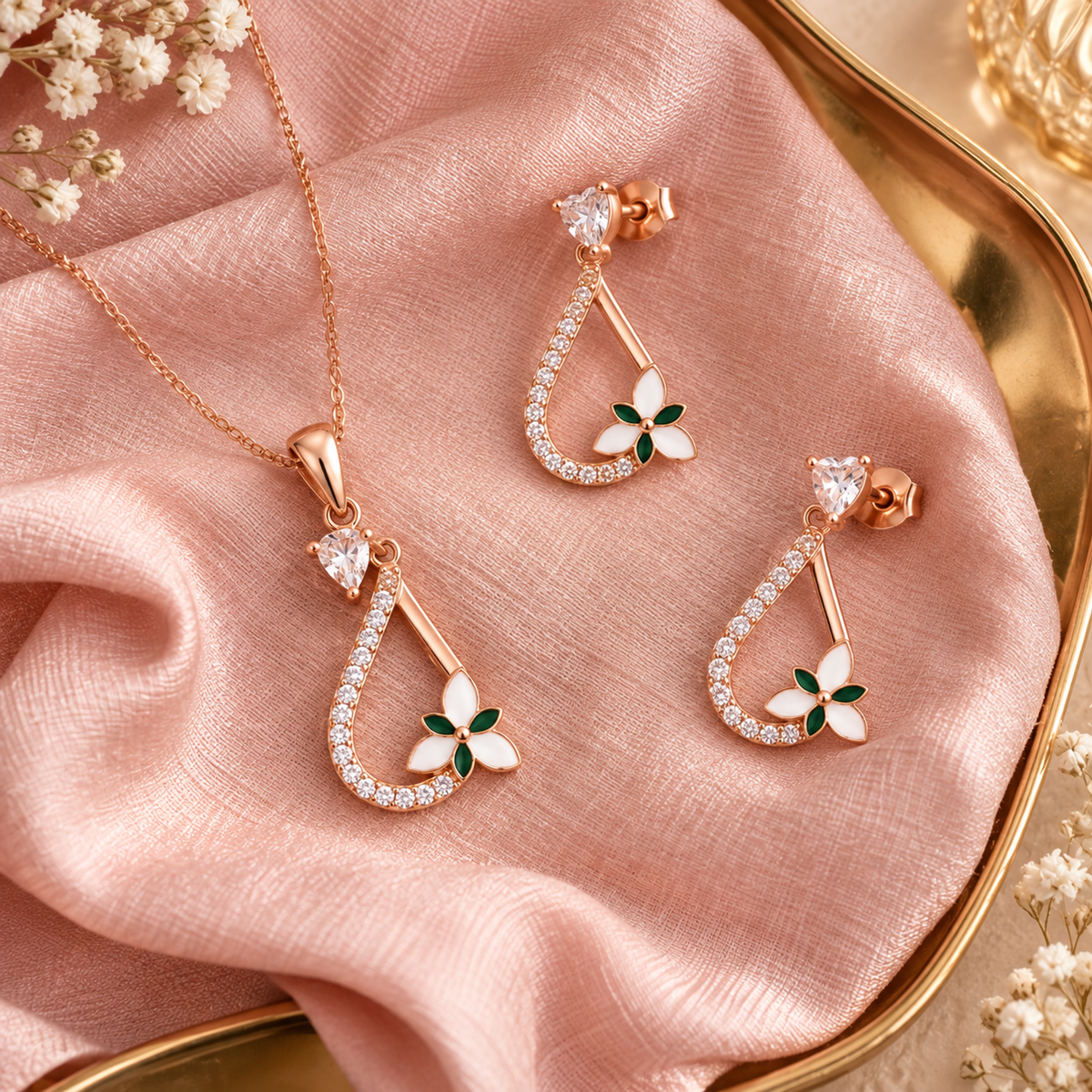 Pendant and two earrings arranged on rumpled blush pink silk over a gold tray.