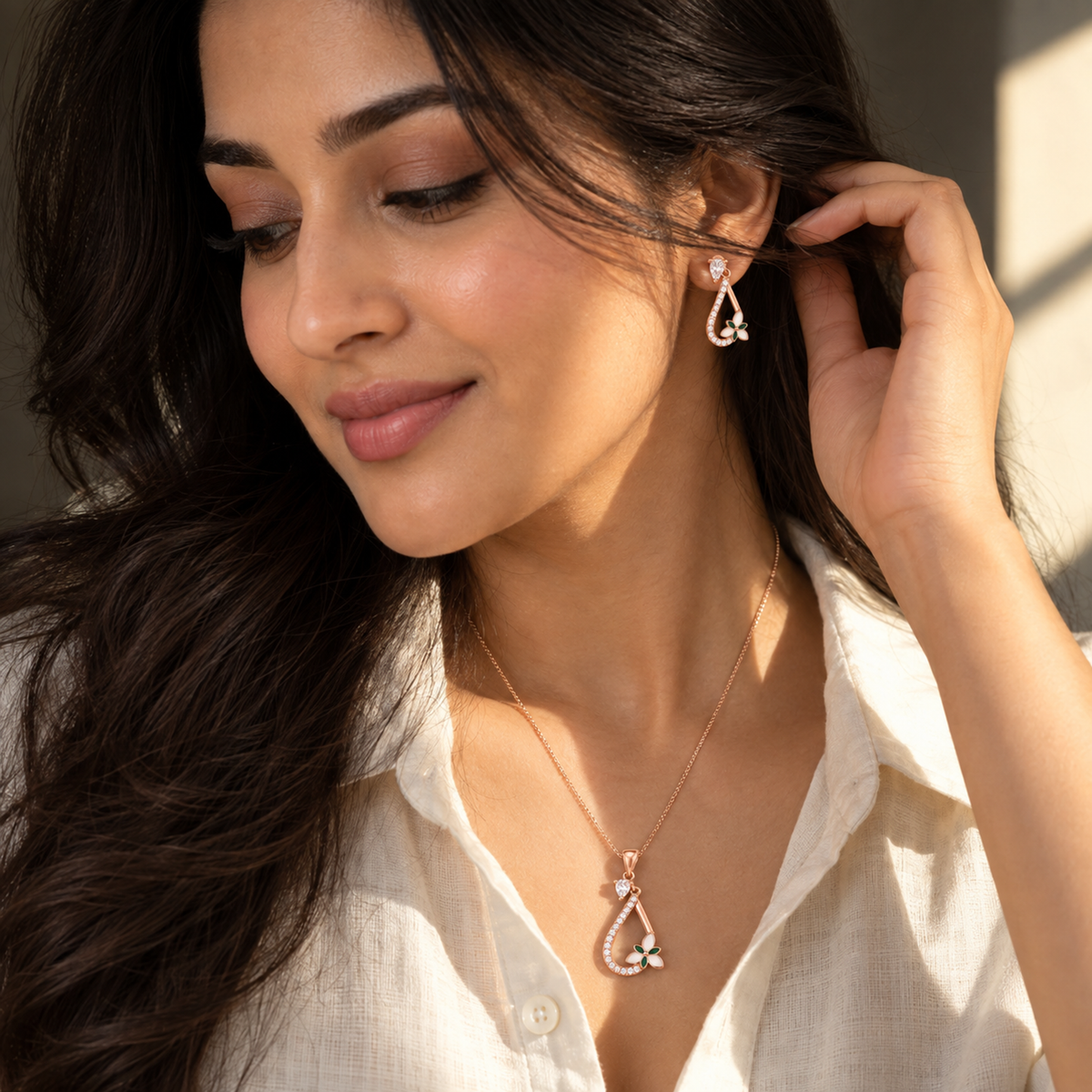 Woman in an ivory shirt tucking hair behind her ear, showing the drop earring.