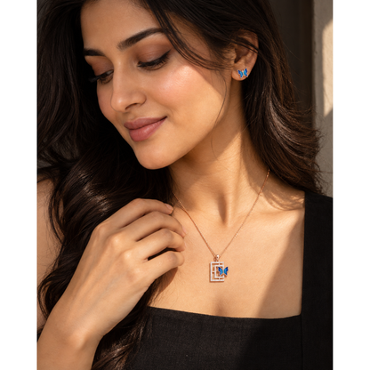 Woman in black top touching the butterfly pendant at her collarbone, eyes lowered.
